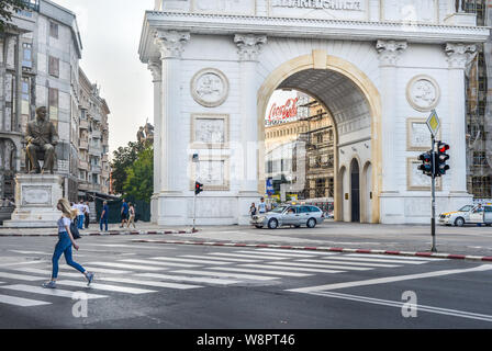 SKOPJE/Mazedonien - 28. AUGUST 2018: Frau durchquert Straße vor Tor von Mazedonien, in der Nähe von Mazedonien entfernt. Stockfoto