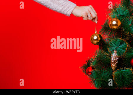 Erntegut Blick auf Frau Hand in Strickpullover glas kugel am Weihnachtsbaum auf rotem Hintergrund Stockfoto