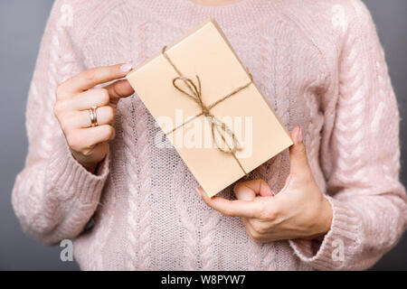 Die Sicht der Frau in weiß Strickjacke Holding wenig verpackte Geschenk auf grauem Hintergrund Stockfoto
