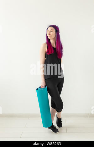 Schlanke junge Mixed Race girl Hipster mit gefärbten Haaren falten Gymnastik Matte nach Yoga im Fitnessstudio. Gesunder Lebensstil und Fitness Concept. Stockfoto