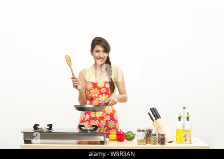 Junge Frau kocht Essen in der Pfanne und lächelt Stockfoto