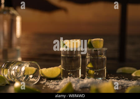 Frische Zitrone Scheiben mit zwei Geschossen von leckeren weißen Tequila und Salz auf den Schwarzen Tisch verstreut. Stockfoto