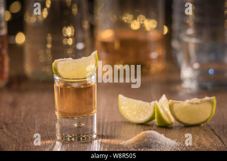 Kalk Schichten auf den Tisch und ein leckeres's Shot tequila mit Tequila Flaschen auf dem Boden und Salz auf dem hölzernen Tisch verstreut - Close-up Stockfoto