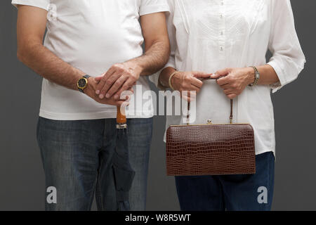 Mittelansicht eines alten Mannes mit Regenschirm und seinem Frau hält eine Handtasche Stockfoto