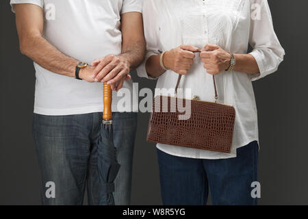 Mittelteil Blick auf einen alten Mann mit Regenschirm und seine Frau hält eine Handtasche Stockfoto