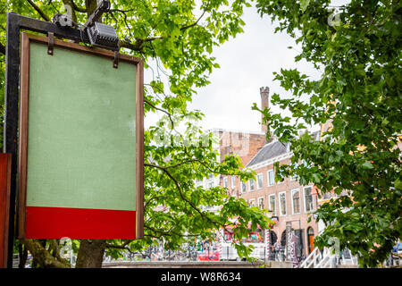 Grüne Brett leer mit Holzrahmen im Freien, blur Gebäude und Bäume Hintergrund. Utrecht, Niederlande, historisches Zentrum. Werbung mockup Vorlage Stockfoto