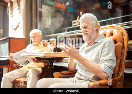 Bärtiger Mann mit Smartphone, während dem Mittagessen mit Freund Stockfoto