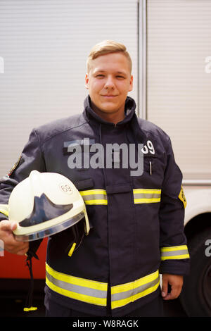 Portrait von Feuerwehrmann mit Helm in der Hand in der Nähe von Feuer-LKW Stockfoto