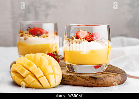 Frontal zwei Glas Gläser mit Desserts von Mango Smoothie, ricotta Käse Sahne, gebackenes Müsli mit Erdbeeren Stücke Stockfoto