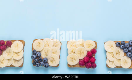 Gesundes Frühstück Sandwiches mit Erdnussbutter, Banane und Beeren auf einem hellen blauen Hintergrund. top Aussicht, Flach, kopieren Raum Stockfoto