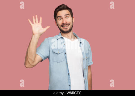 Hallo, schön, dich zu sehen. Portrait von überrascht gut aussehender bärtiger junger Mann im blauen style Shirt stehen und an der Kamera mit toothy Lächeln und greetin Stockfoto