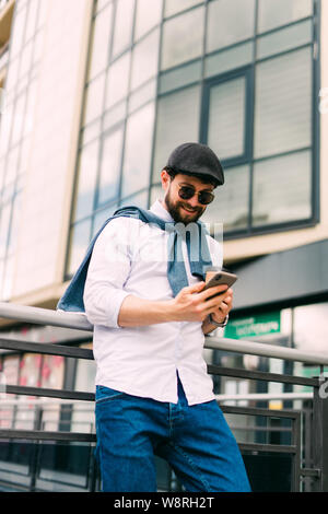Closeup Schoß des jungen Mannes Messaging auf dem Smartphone. Glücklich lächelnde businessamn bei smart phone lehnte sich gegen ein Geländer im Freien suchen. Hübscher junger Stockfoto