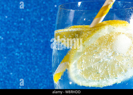 Frisch Soda mit Blasen einen Eiswürfel, einer Scheibe Zitrone und ein Stroh auf einem glänzenden blauen Hintergrund Stockfoto