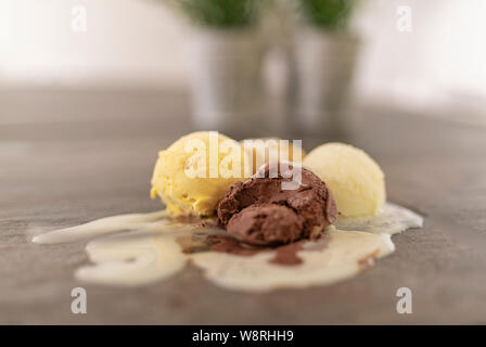 Eine Kugel aus Schokolade zusammen mit drei leckeren Kugeln Eis mit Sahne zerdrückt, Schmelzen auf einem Tisch aus Stein - lecker Eis - in der Nähe Stockfoto