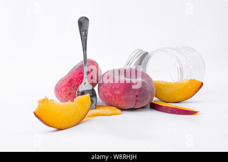 Zwei flache Pfirsiche von Scheiben und ein Glas Glas - auf einem weißen Hintergrund - gelbe Scheiben begleitet Stockfoto