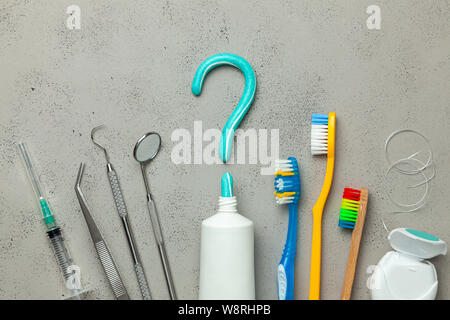 Zahnpasta in Form eines Fragezeichens und viele verschiedene und farbigen Zahnbürsten und Zahnseide, Dental Werkzeug. Konzept der, wie man die richtige Zahnbürste oder wie Sie Ihre Zähne zu putzen. Stockfoto