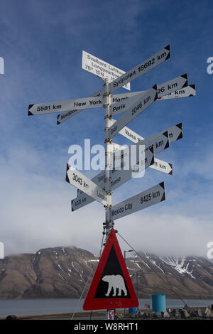 Ein Wegweiser, der die Entfernungen zu Städten und Städten in aller Welt vom Flughafen Svalbard, Longyearbyen, Svalbard anzeigt, mit einem Eisbären-Warnschild unten. Stockfoto