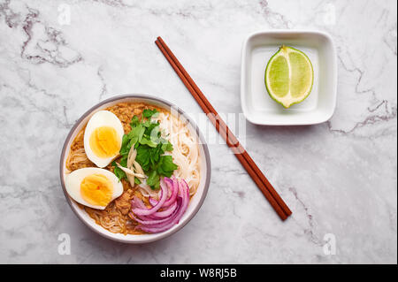 Mohinga auf weißem Hintergrund. Mohinga ist eine burmesische Küche Fischsuppe mit Wels, Reisnudeln, Huhn Eier und Kalk. Stockfoto