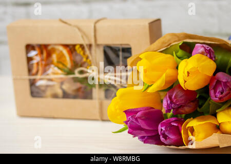 Ein Geschenk mit Süßigkeiten in Kraft Verpackung und einen Strauß gelb lila Tulpen im Kraftpapier, ein Geschenk für eine Frau auf einem weißen Hintergrund Stockfoto