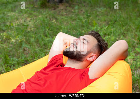 Ein junger Mann mit einem Bart liegt mit seinen Augen auf eine Orange aufblasbare Sofa geschlossen. Der Reisende oder touristische ruht in der Natur. Stockfoto