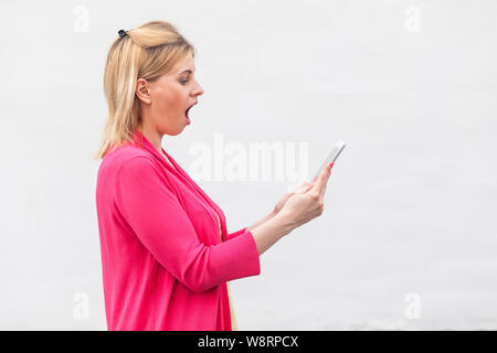 Auf keinen Fall! Seitenansicht Portrait von unglaublich junge Frau in rosa Bluse stehen und beobachten überrascht Video auf Ihrem Tablet-PC mit entsetzten Gesicht. Indoor, ist Stockfoto