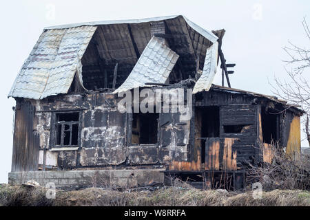 Verbrannte Holz- Haus, schwarz verkohlte Skelett eines Landhauses. Verkohlte Stämme blieben aus dem Dorf Haus. Verkohlte Mauern, leere Fenster und hohlen r Stockfoto