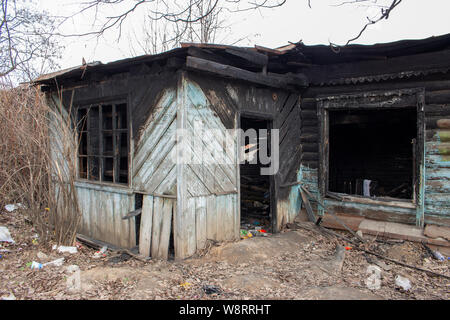 Country House nach dem Brand. Das Skelett einer verbrannten Holz- Haus. Gebrochene Verkohlten Wohnung. Zerbrochene Scheiben in der Tür, schwarze Wände, Feuer Unglück Stockfoto
