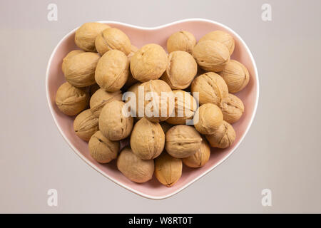 Die Walnüsse in einer herzförmigen Platte. Die Muttern Herz, Herz Gesundheit Produkte, Strukturierte Walnüsse Gesunde Ernährung Protein Stockfoto