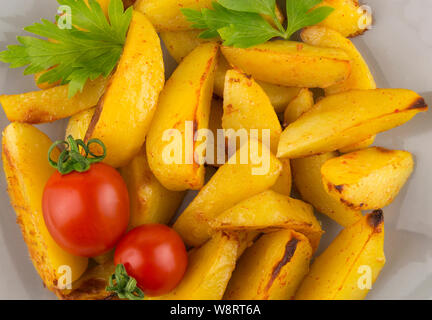 Stücke von Kartoffel gebacken in einem Land Stil mit kleinen reifen Tomaten und Petersilie serviert. Gebackene Kartoffeln mit Gemüse, essen Foto - Ansicht von oben Stockfoto
