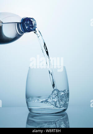 Sauberes, frisches, kühles Trinkwasser fliesst aus einem Kunststoff blau Flasche in eine transparente, sauber, bauchigen Glas mit schönen Blasen. Ein Wasserstrahl wit Stockfoto