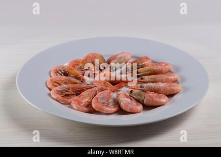 Aufgetaut gekochte Garnelen Garnelen Hummer sind auf einem weißen Teller. Raw kleine rosa Garnelen in der Schale mit Kopf und Schwanz, shell Lebensmittelzutat vorgefertigt Stockfoto