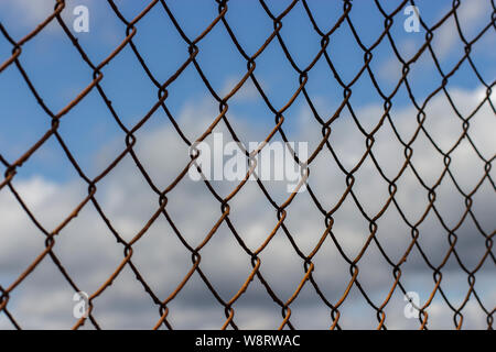 Alte rostige Gitter diagonal Verrechnung gegen einen blauen Himmel mit Wolken, Hintergrund Textur. Rost auf einen Metallzaun in einem Käfig Stockfoto