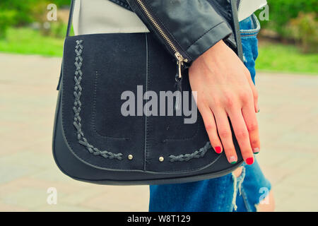 Junge Frau halten yoyr Hand über die schwarze Handtasche auf der Schulter tragen Rip-jeans Taille ebene Seitenansicht Schuß getönten in Vintage Farben Stockfoto