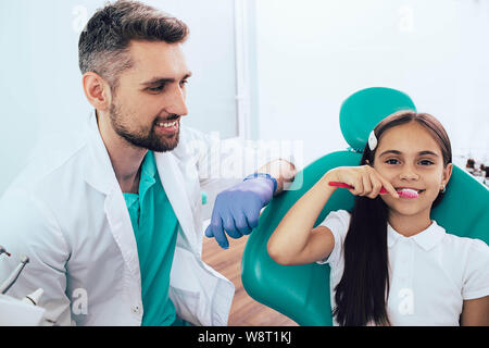 Zahnarzt Lehre wenig gemischten Rennen Mädchen Zähneputzen mit menschlichen Zähne Modell auf zahnmedizinische Klinik Stockfoto