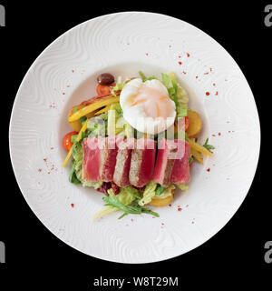 Nicoise Salat von seltenen gebratener Thunfisch, Kartoffel, Salat Mix und pochiertem Ei in weiße Platte, isoliert auf Schwarz Stockfoto