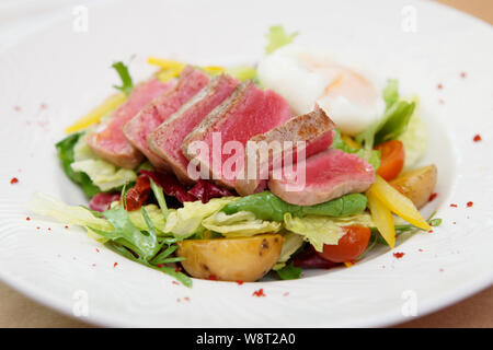 Nicoise Salat von seltenen gebratener Thunfisch, Kartoffel, Salat Mix und pochiertem Ei in weiße Platte Stockfoto