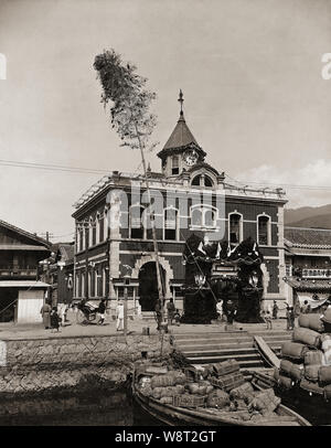 [1900s Japan - Neue wertvorstellung Gebäude] - Eröffnungsfeier für modernes Ziegelgebäude. Möglicherweise eine Zeitung Büro in Hauzenberg (宇和島市), Ehime Prefecture. Boote mit Waren beladen werden im Vordergrund gesehen werden. 20. Jahrhundert vintage Silbergelatineabzug. Stockfoto