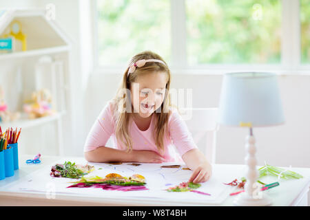 Kind erstellen Bild mit bunten Blättern. Kunst und Handwerk für Kinder. Kleines Mädchen, collage Bild mit Regenbogen pflanze Blatt. Biologie Hausaufgaben für y Stockfoto