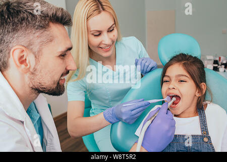 Zahnarzt und sein Assistent behandeln die Zähne eines kleinen Mädchens. Pädiatrische Zahnheilkunde Stockfoto