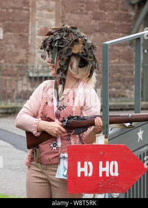 Fort George, Inverness, Schottland, 10. August 2019. Weibliche Besucher Tragen eines militärischen Helm mit Camouflage Material und halten ein WWII Gewehr. Das historische Schottland Festival am Fort Ereignismarkierung 250 Jahre Fort George. Stockfoto