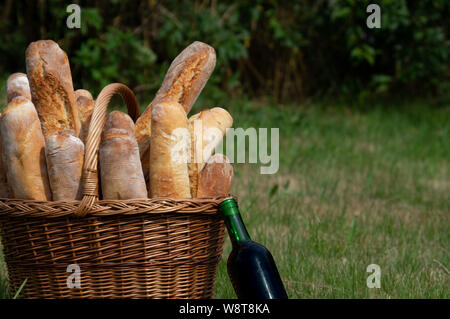 Frisches Brot in einem Korb mit einer Flasche Rotwein auf einer Wiese Stockfoto