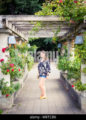 Eine hübsche Brünette Mädchen unter eine Laube von Rosen in der UBC Rosengarten (Universität von Britisch-Kolumbien Rosengarten) in Vancouver, BC, Kanada. Stockfoto