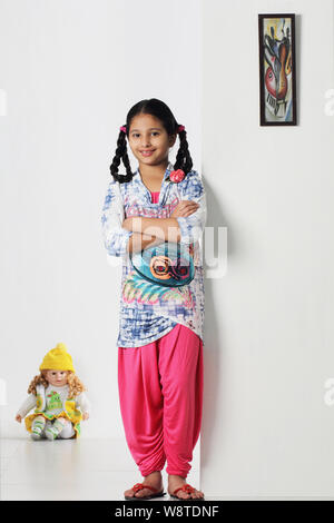 Mädchen mit ihre Arme verschränkt mit einer Puppe im Hintergrund stehen Stockfoto