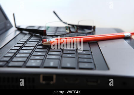 Bleistifte und Brillen auf der Tastatur auf dem Laptop Stockfoto