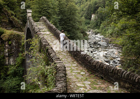 Ein fünfzehnjähriger Junge überquert die Römische Brücke (Ponte Romano) auf der Melezza bei Intragna im italienischen Tessin in der Schweiz. Stockfoto