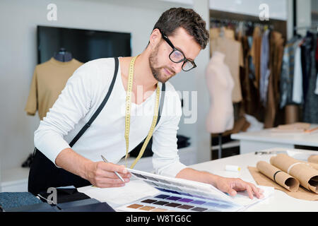 Junge männliche Designer Mode bei Textile Proben im Katalog suchen Stockfoto