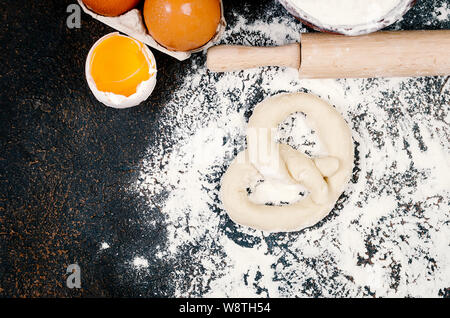 Raw Brezel und Zutaten, Eier, Mehl, Ähren auf dunklen Küche Tisch, frisch gebackenem Brot Teig auf aflour fertig gebacken werden. Vorbereitung der b Stockfoto