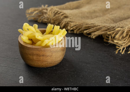 Menge ganze rohe Nudeln Gemelli in Houten mit Jute-stoff auf grauem Stein Stockfoto