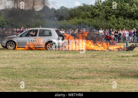 Scott May’s Daredevil Stunt Show in Rayleigh, Essex, Großbritannien. Das Auto zerrt einen Stuntman durch das Feuer. Flammen Stockfoto