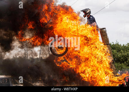 Scott May’s Daredevil Stunt Show in Rayleigh, Essex, Großbritannien. Motorradfahrer springt durch das Feuer. In Flammen mit schwarzem Rauch Stockfoto